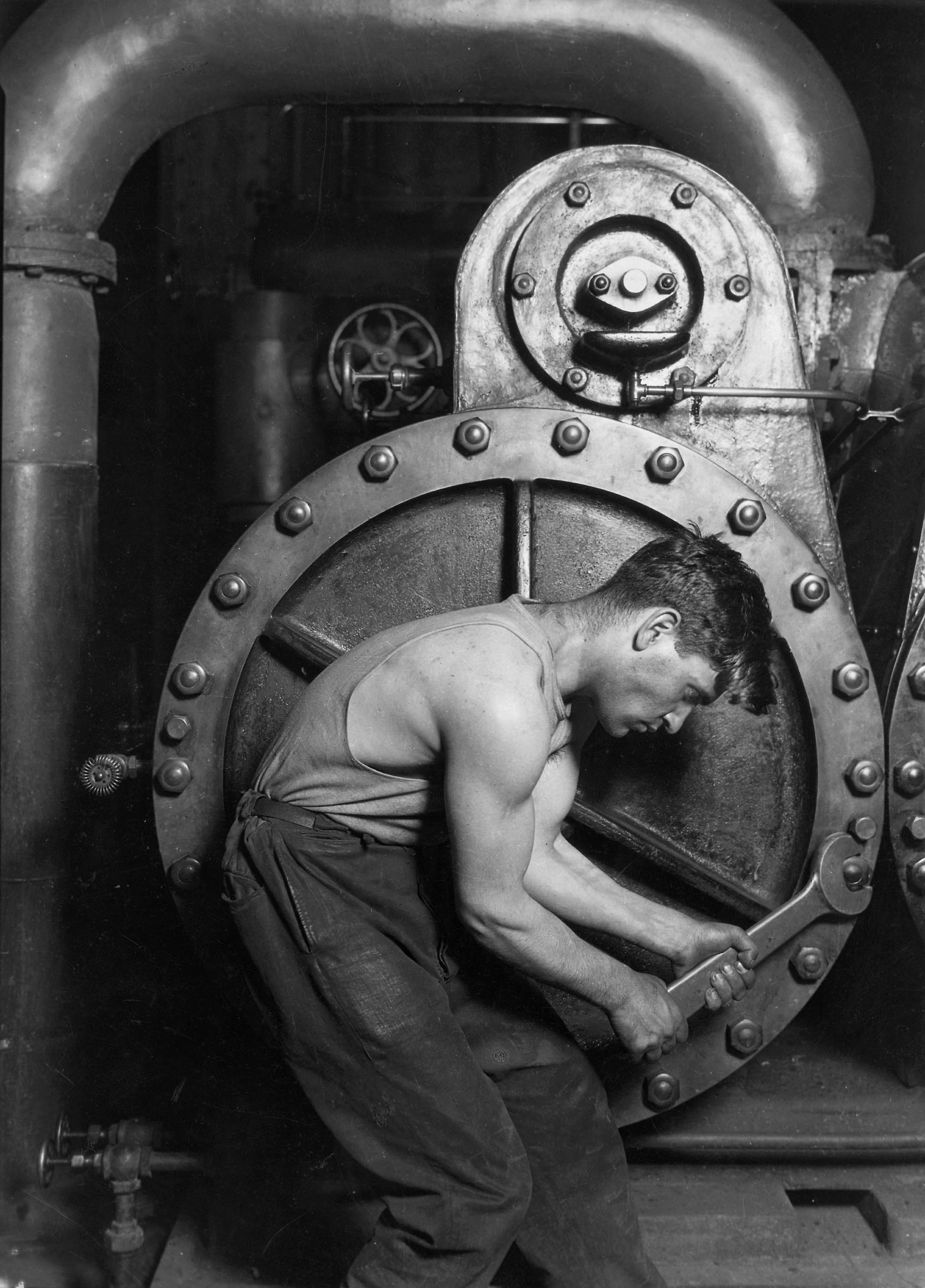 A mechanic, wrench in hand, bent over the machinery of a steam pump